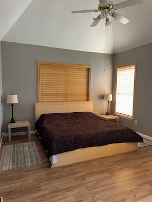Una camera da letto con un letto, due comodini, una ventola a soffitto e due finestre con tende.