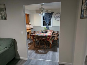 A dining area with a table, chairs, a ceiling fan, and a window with curtains.