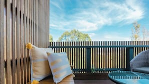 A wooden deck with a cushioned bench and a wicker chair, a wooden fence, and a clear sky. - Cosy container house walking distance to town. (Korumburra)
