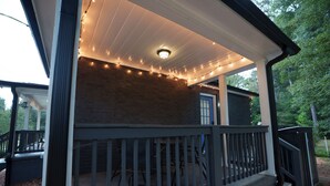 A covered porch with a brick wall, wooden railing, and string lights. - Luxury 4BR 4BA • In-law suite • Firepit Lounge (Decatur)