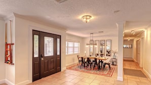 A spacious dining area with a large wooden table and chairs, a patterned rug, and a chandelier.