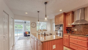 A kitchen with wooden cabinets, granite countertops, a stainless steel range hood, and pendant lighting.