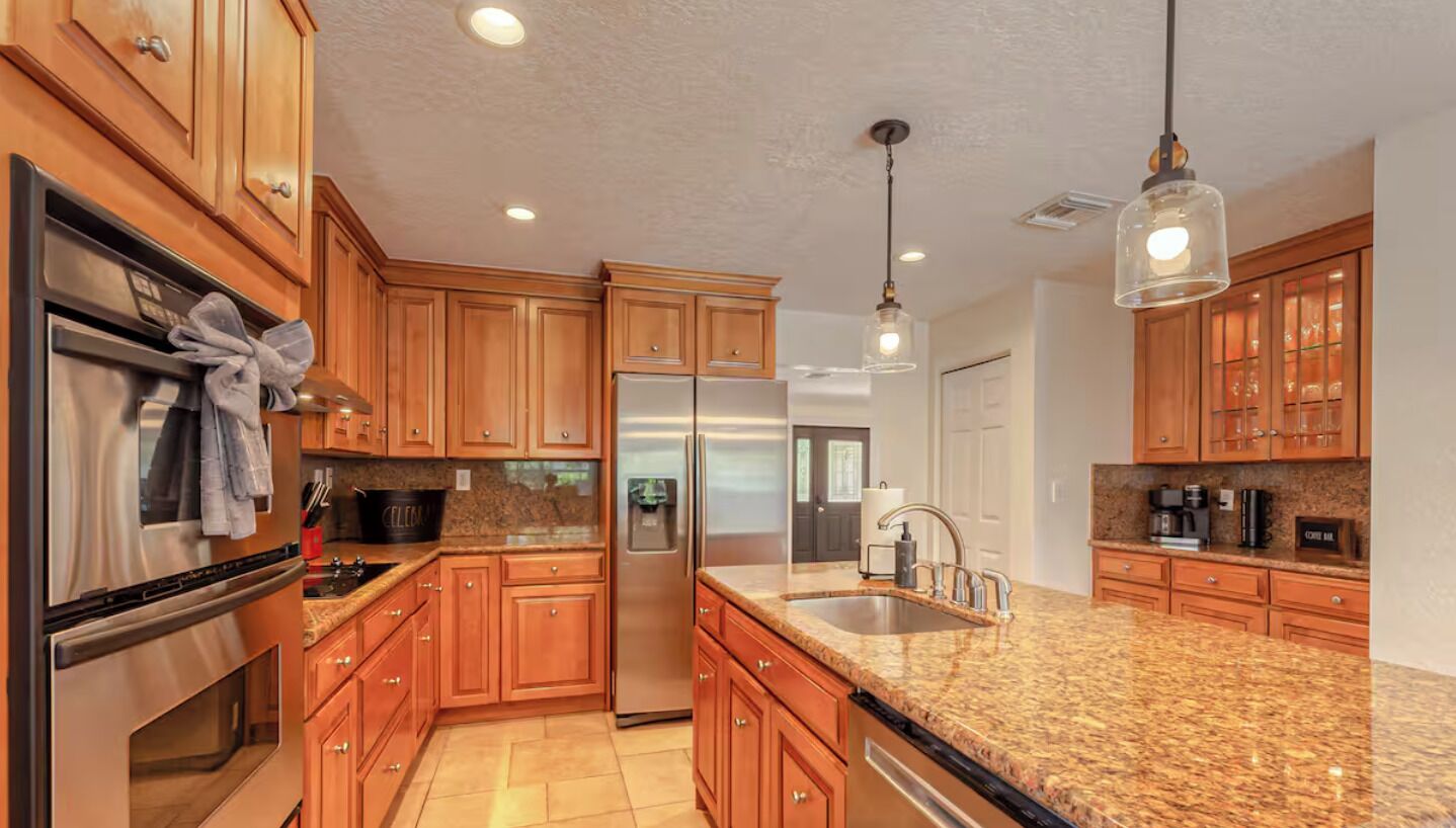 A modern kitchen with wooden cabinets, stainless steel appliances, granite countertops, and pendant lighting.