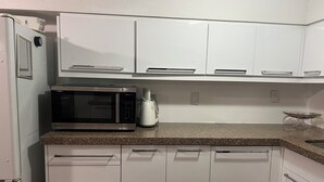 Una cocina con armarios blancos, microondas de acero inoxidable y cafetera.