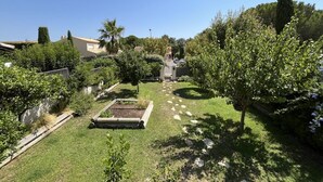 Un jardín bien cuidado con un parterre central, rodeado de arbustos y árboles diversos.
