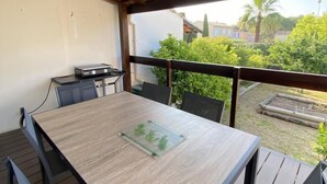 Un espacio de patio cubierto con mesa y sillas de madera, una parrilla y vistas a zonas verdes y edificios.
