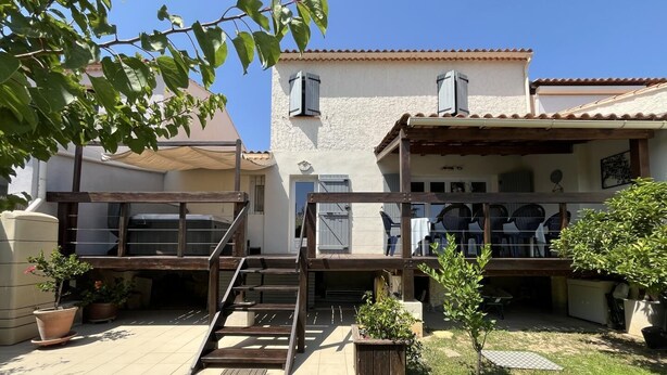 Una casa de dos pisos con un patio, mobiliario exterior y un pequeño jardín.
