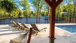 Ett område vid poolen med solstolar, en hängmatta och utsikt över en sjö och hus.
