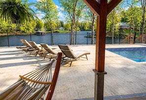 Un área junto a la piscina con sillones reclinables, una hamaca y vistas a un lago y casas.