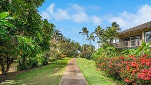 A pathway leading to a building with a balcony, surrounded by lush greenery and tropical plants.