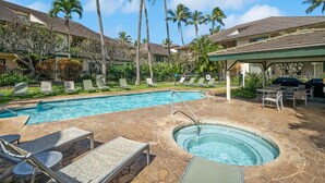 A hotel pool area with lounge chairs, a hot tub, and palm trees.