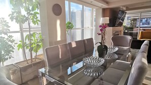 A modern dining area with a glass table, cushioned chairs, and a view of the city through large windows. - Suites Cusco (Cusco)