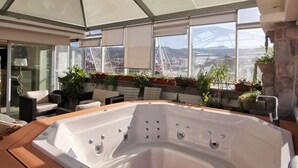 A modern indoor hot tub area with a glass ceiling, a wooden deck, and a view of a bridge and cityscape. - Suites Cusco (Cusco)