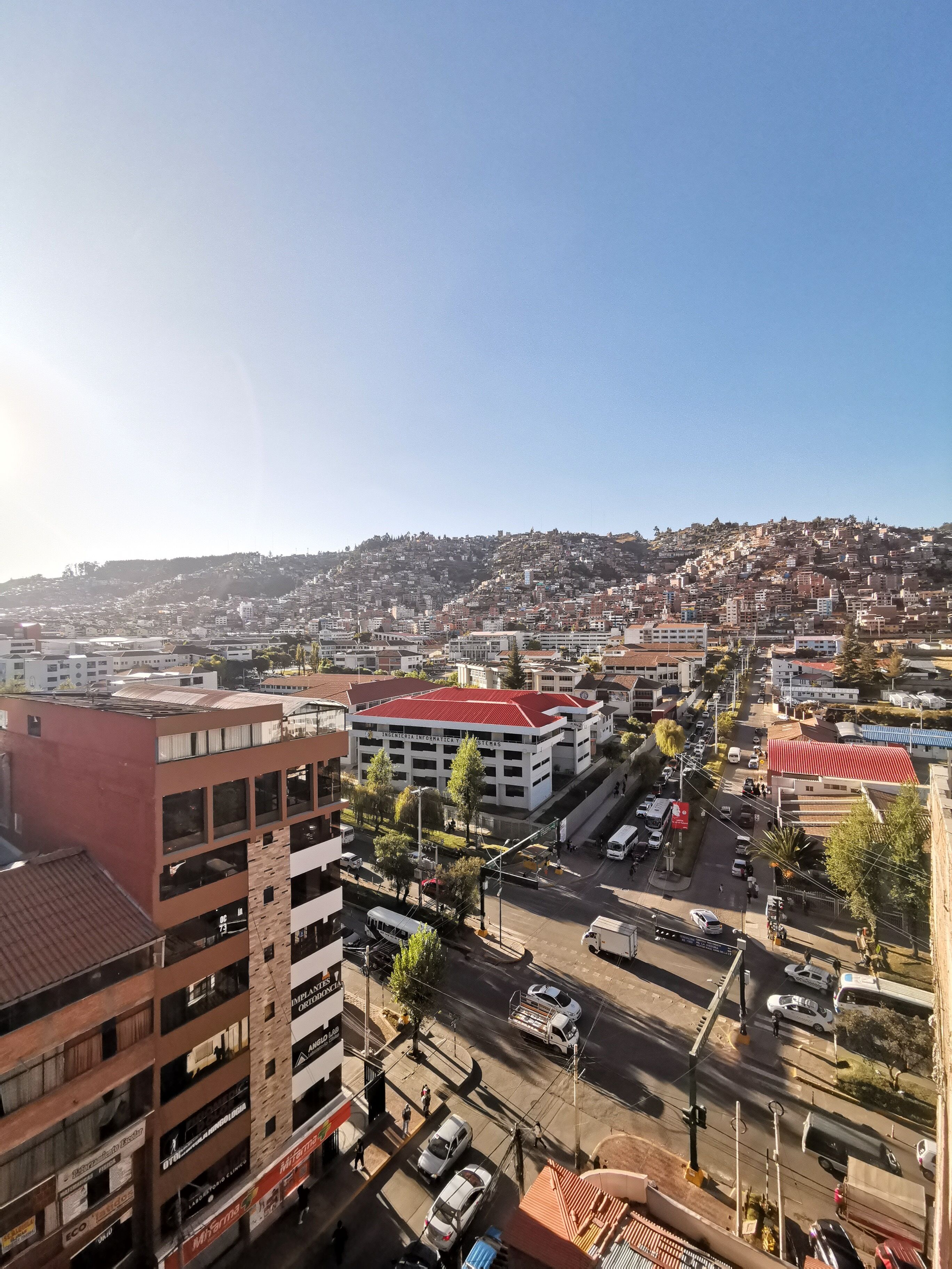 A cityscape with a prominent building with a red roof and multiple floors, surrounded by other buildings and streets.