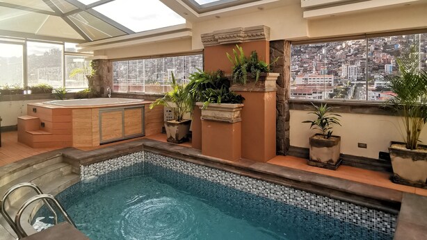 A rooftop swimming pool with a glass ceiling, stone steps, and potted plants. - Suites Cusco (Cusco)