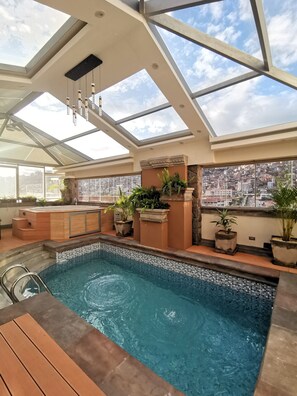 A rooftop swimming pool with a glass ceiling, stone steps, and potted plants. - Suites Cusco (Cusco)