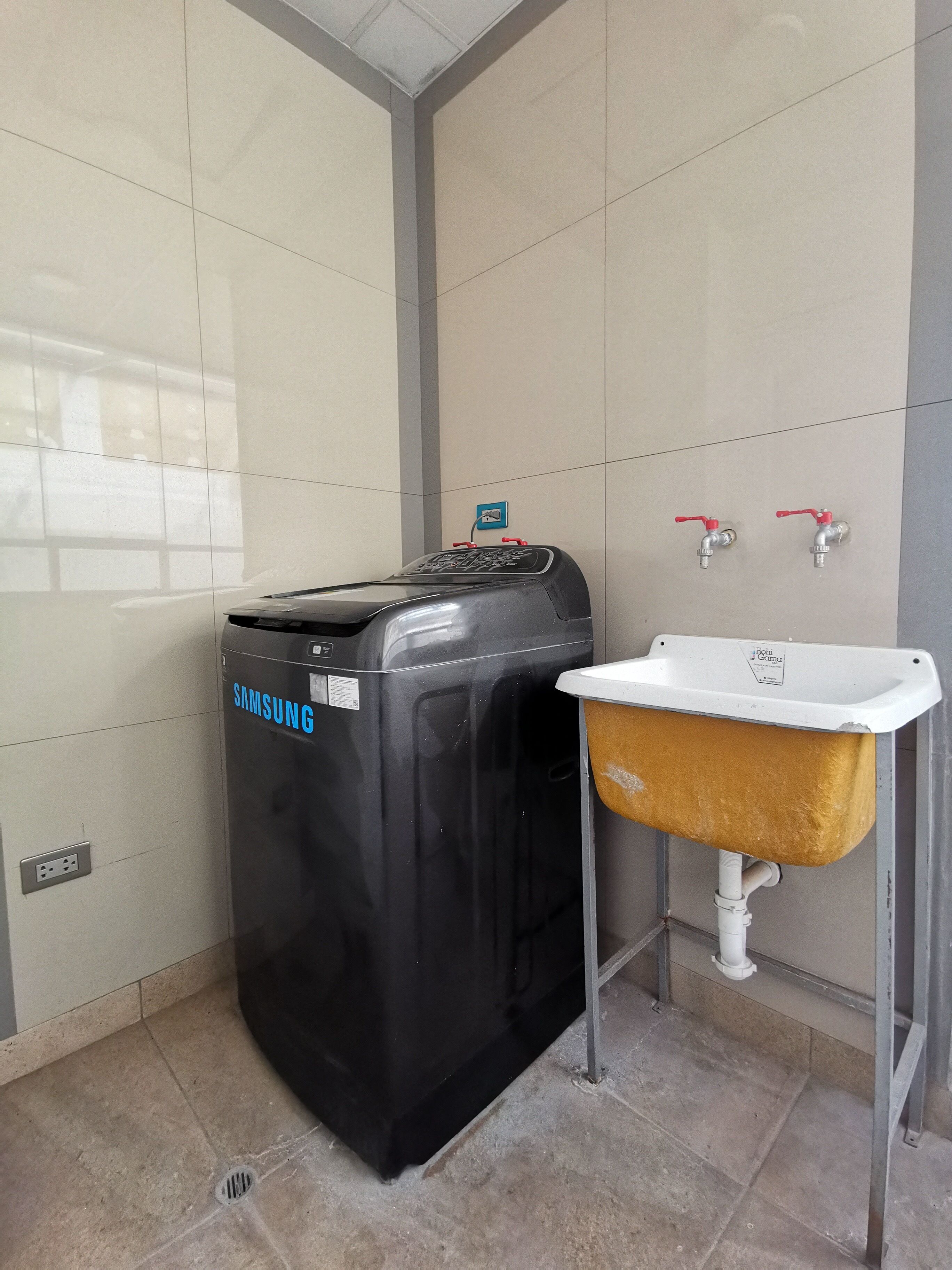 Une salle de bain équipée d’un lave-linge Samsung, d’un évier et de deux robinets.