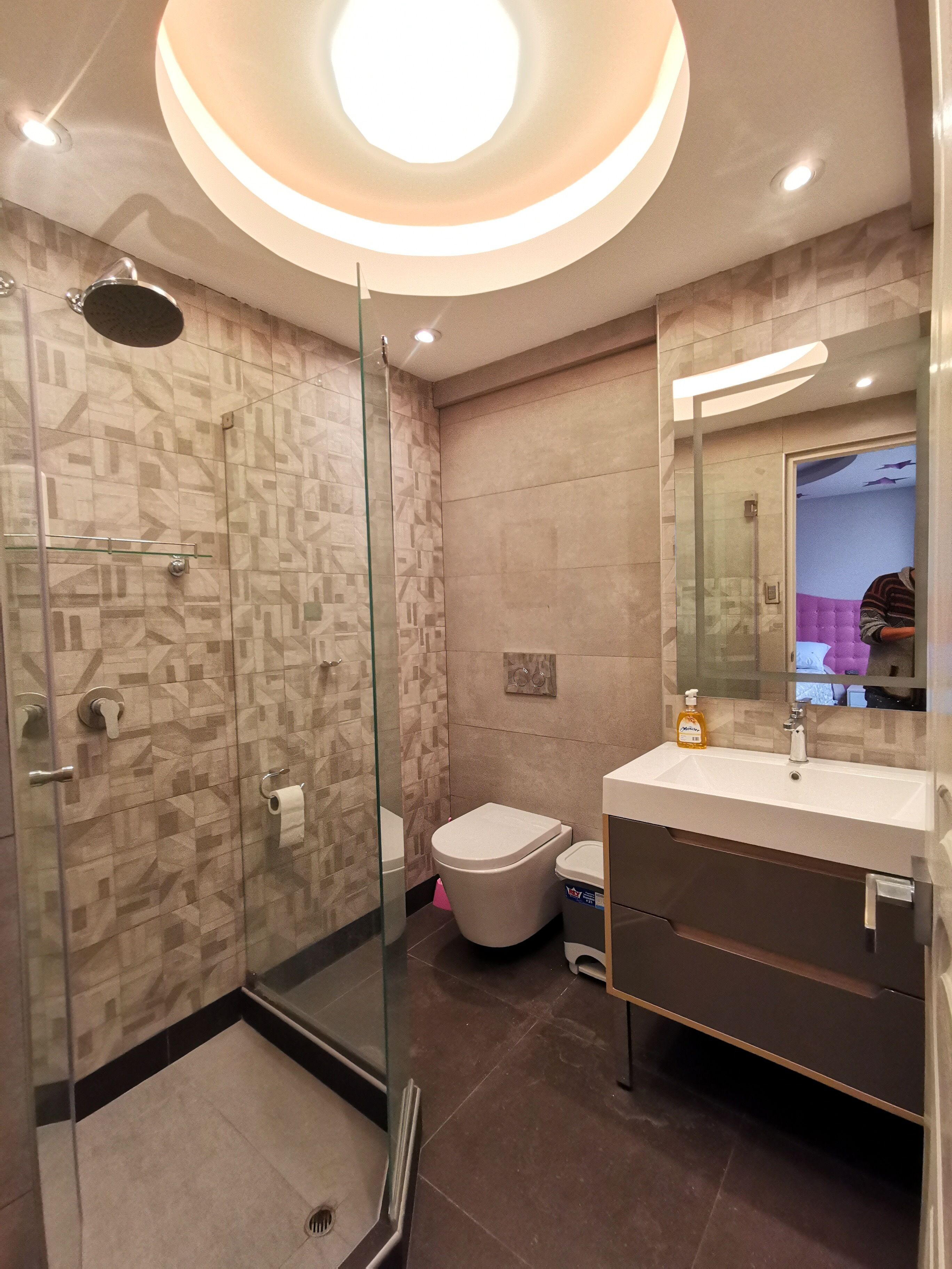 A modern bathroom with a glass-enclosed shower, a toilet, and a vanity with a mirror.