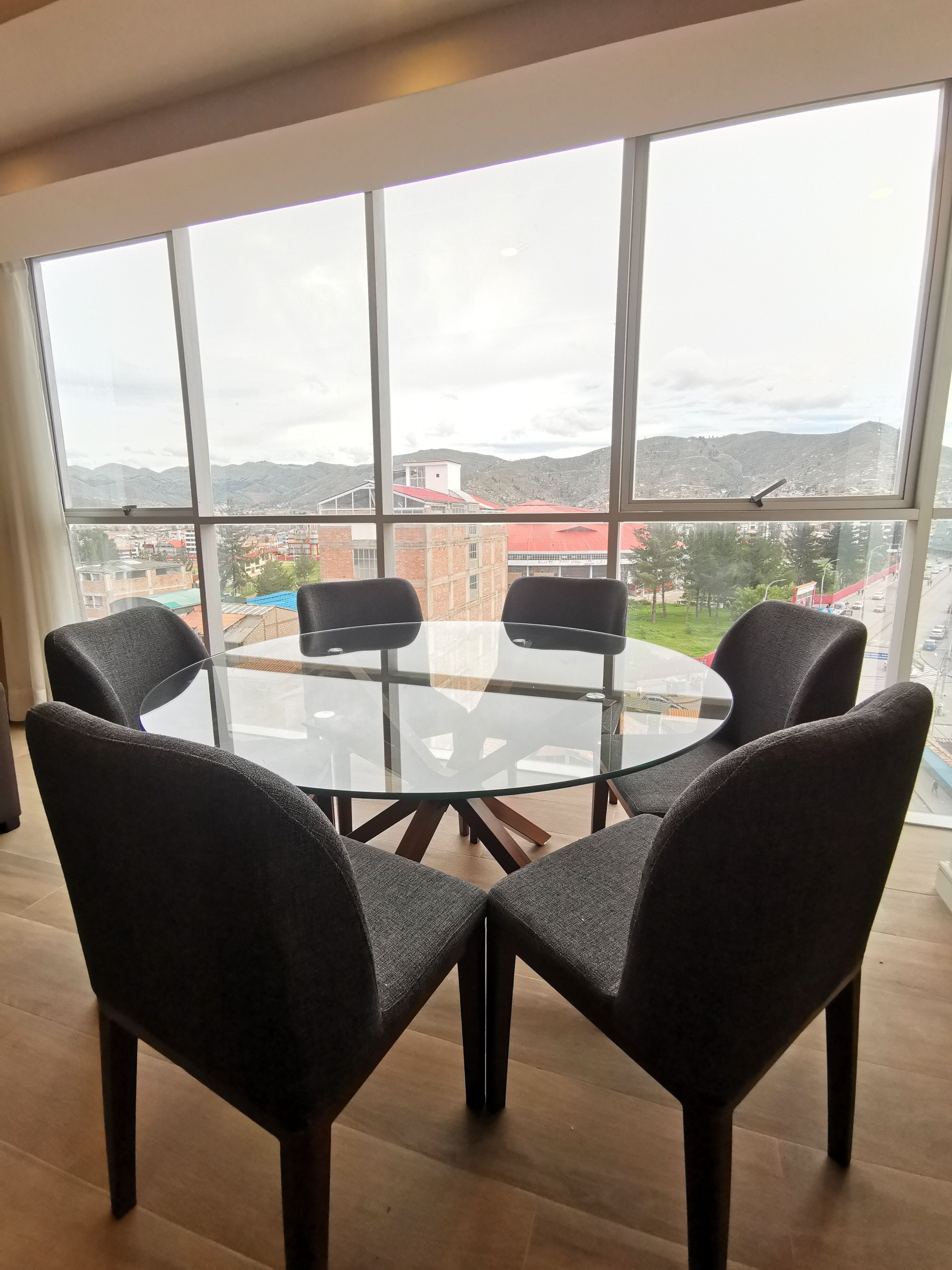 A room with a large window, a round glass table, and four dark chairs.
