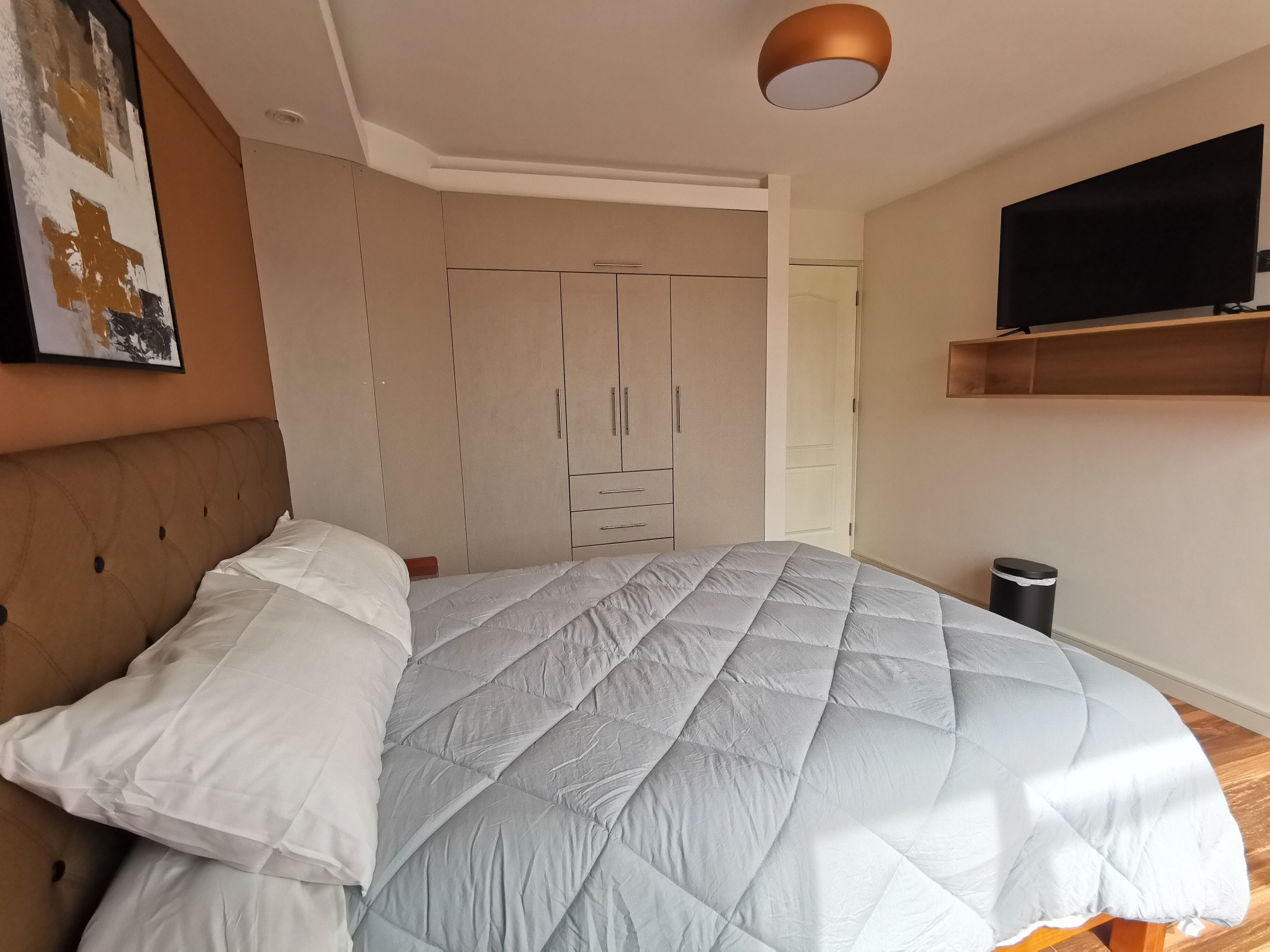 A bedroom with a bed, a wardrobe, a television, and a trash bin.