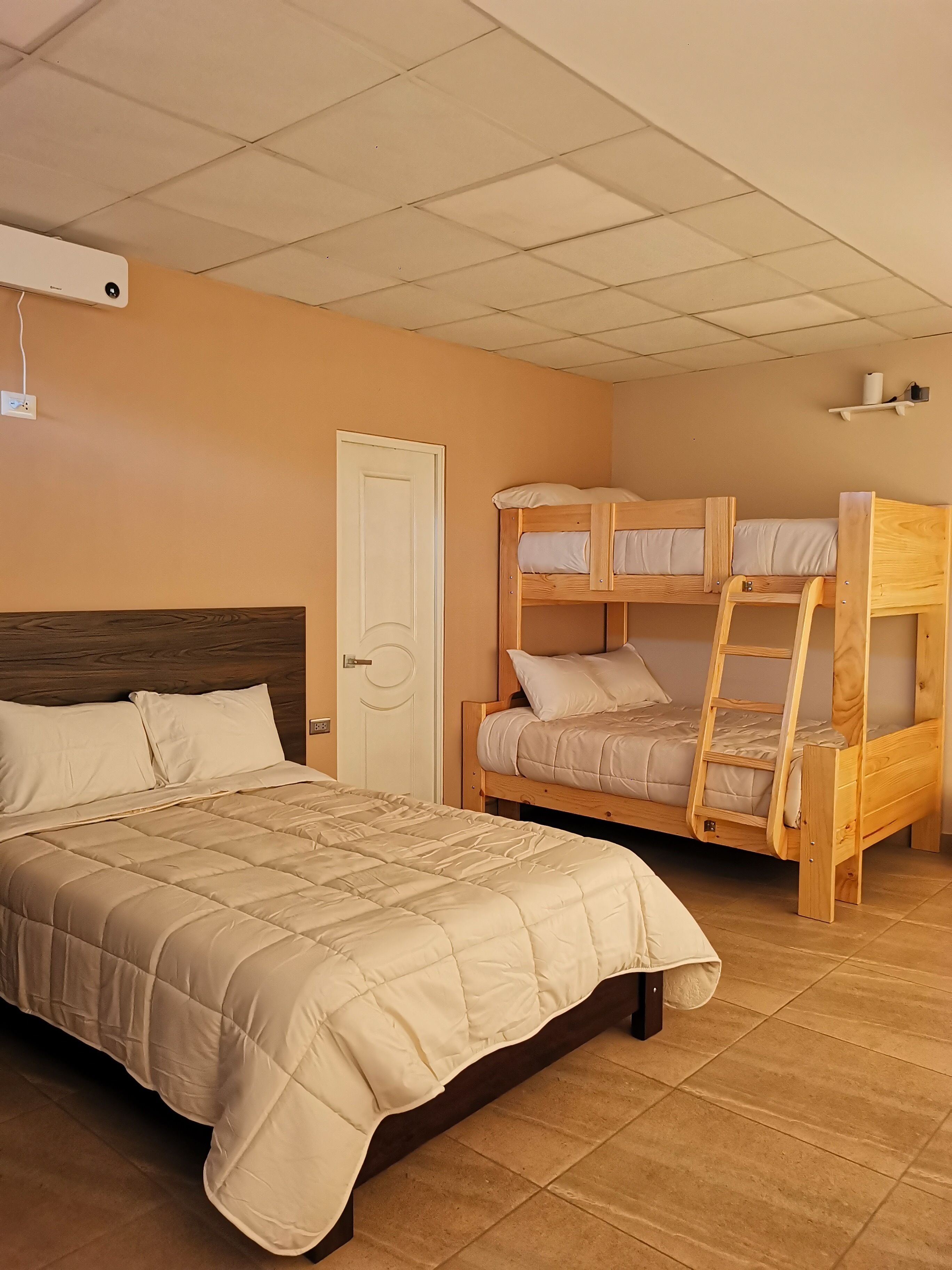 Une chambre avec un grand lit, un lit superposé et une porte.