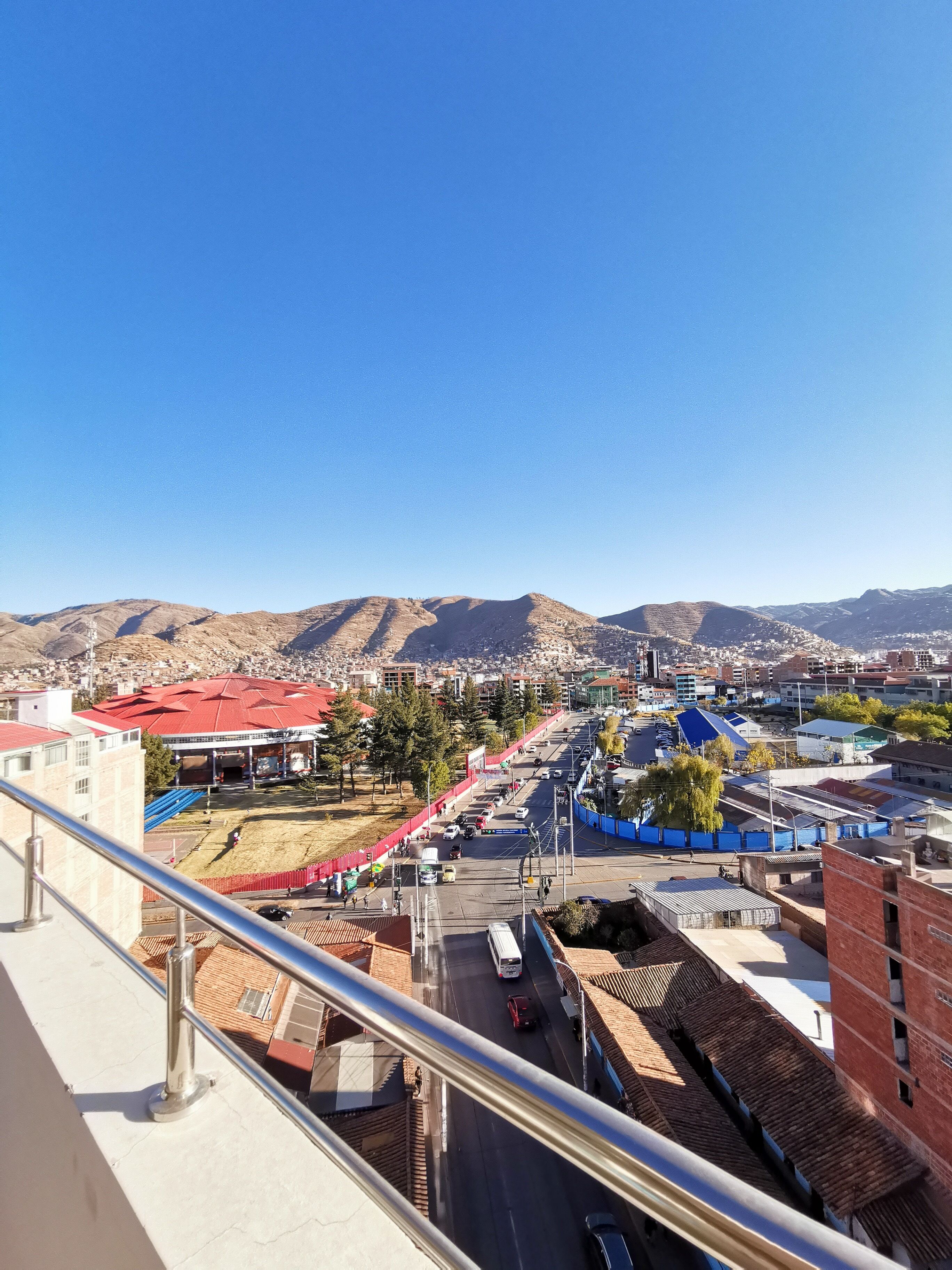 A cityscape with a prominent red-roofed building, a clear blue sky, and distant mountains.