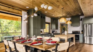 A modern kitchen with wooden cabinets, a stainless steel refrigerator, and a dining area with a wooden table and chairs. - Chara Vista Cabin: A Smoky Mountain Retreat (Sevierville)