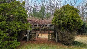 A wooden arbor with a lattice top, surrounded by evergreen and deciduous trees. - Features two living rooms, sauna, hot tub, and fire pit -over 4 acres of land. (Stroudsburg)