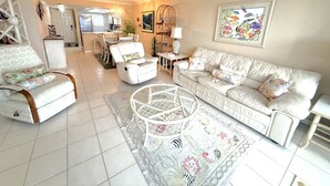 Ein geräumiges Wohnzimmer mit einem weißen Ledersofa, einem passenden Sessel und einem Couchtisch. Im Hintergrund ist eine Essecke mit Tisch und Stühlen zu sehen.