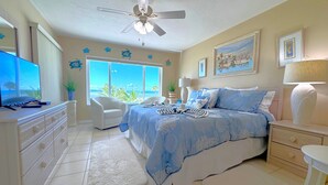 Ein Schlafzimmer mit Bett, Schreibtisch, Stuhl, Deckenventilator und Meerblick.