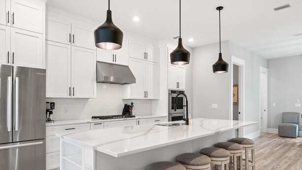 Una cucina moderna con mobili bianchi, elettrodomestici in acciaio inossidabile, una grande isola con sgabelli e luci a sospensione.