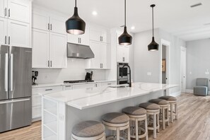 A modern kitchen with white cabinets, stainless steel appliances, a large island with stools, and pendant lighting. - 💎 Inlet Jewel | Rooftop Entertainment Deck & Hot Tub | Stunning Views ☀️ (Inlet Beach)