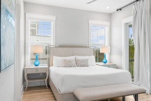 Ein Schlafzimmer mit einem Bett, zwei Nachttischen, einer Bank und zwei Fenstern mit Jalousien.
