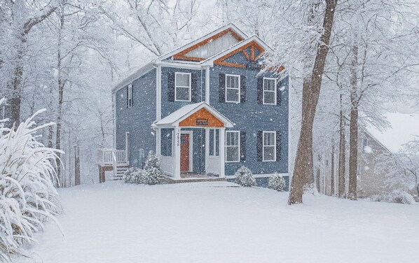 A two-story house with a porch, surrounded by snow-covered trees. - Mountain Dreams (Massanutten)