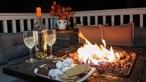 Une table sur laquelle sont disposés un plateau de guimauves, du chocolat et une bouteille de champagne, le tout installé sur un balcon avec un feu de cheminée et un canapé en arrière-plan.