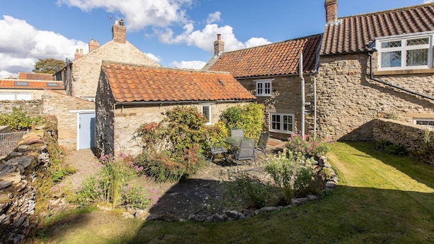 A stone house with a tiled roof, a small garden, and a visible window.