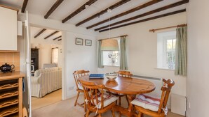 A dining area with a wooden table and chairs, a bookshelf, and a view into the kitchen.