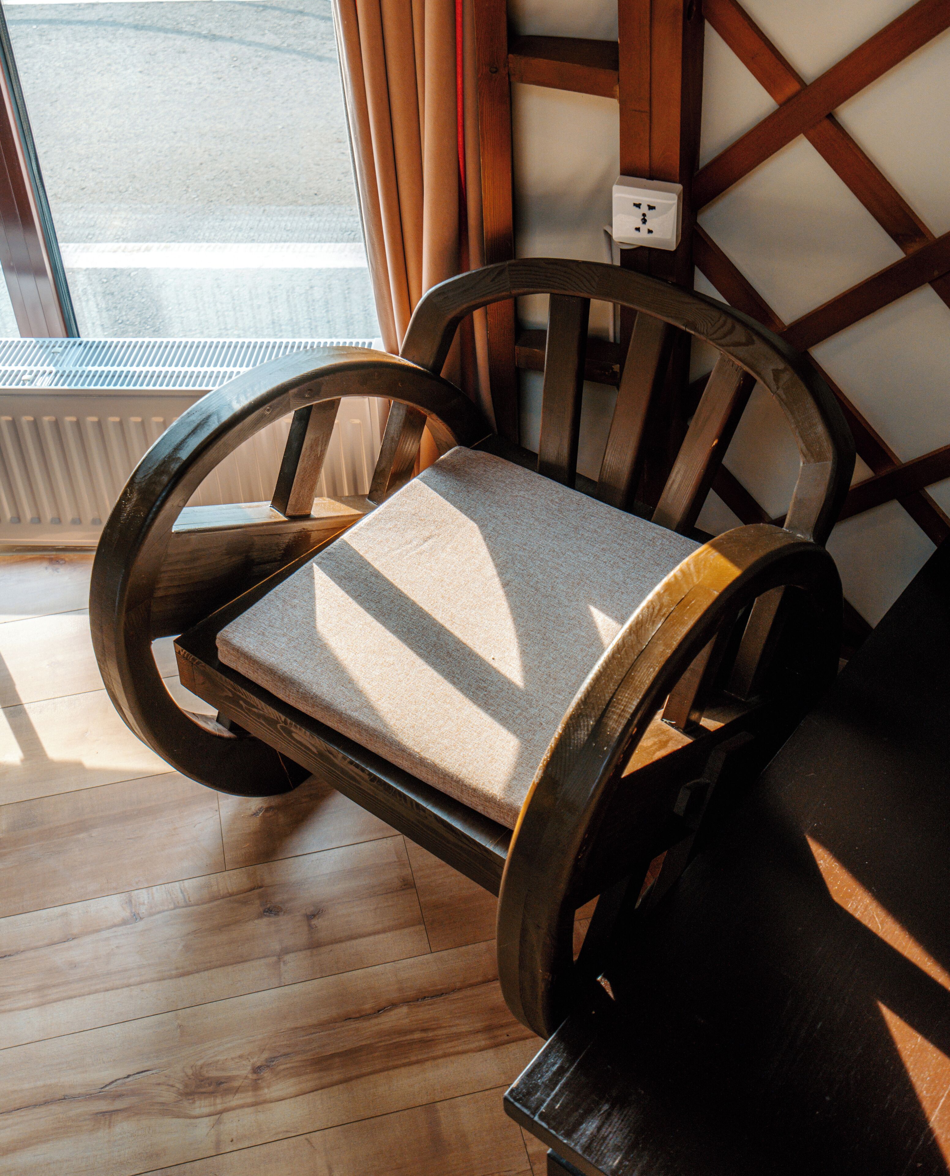 Una silla de madera con asiento y respaldo acolchados, ubicada en un interior con vistas a una ventana y un radiador.