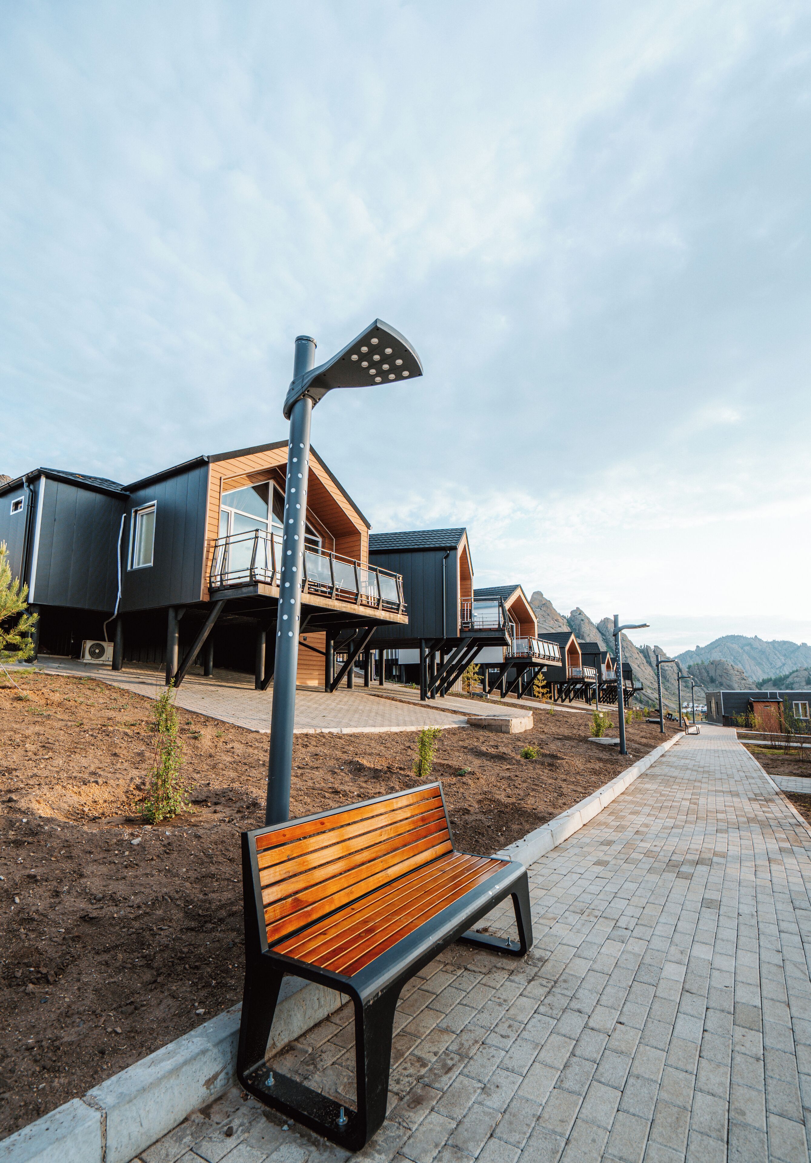 A row of modern, multi-level cabins with outdoor balconies, a paved walkway, and a bench.