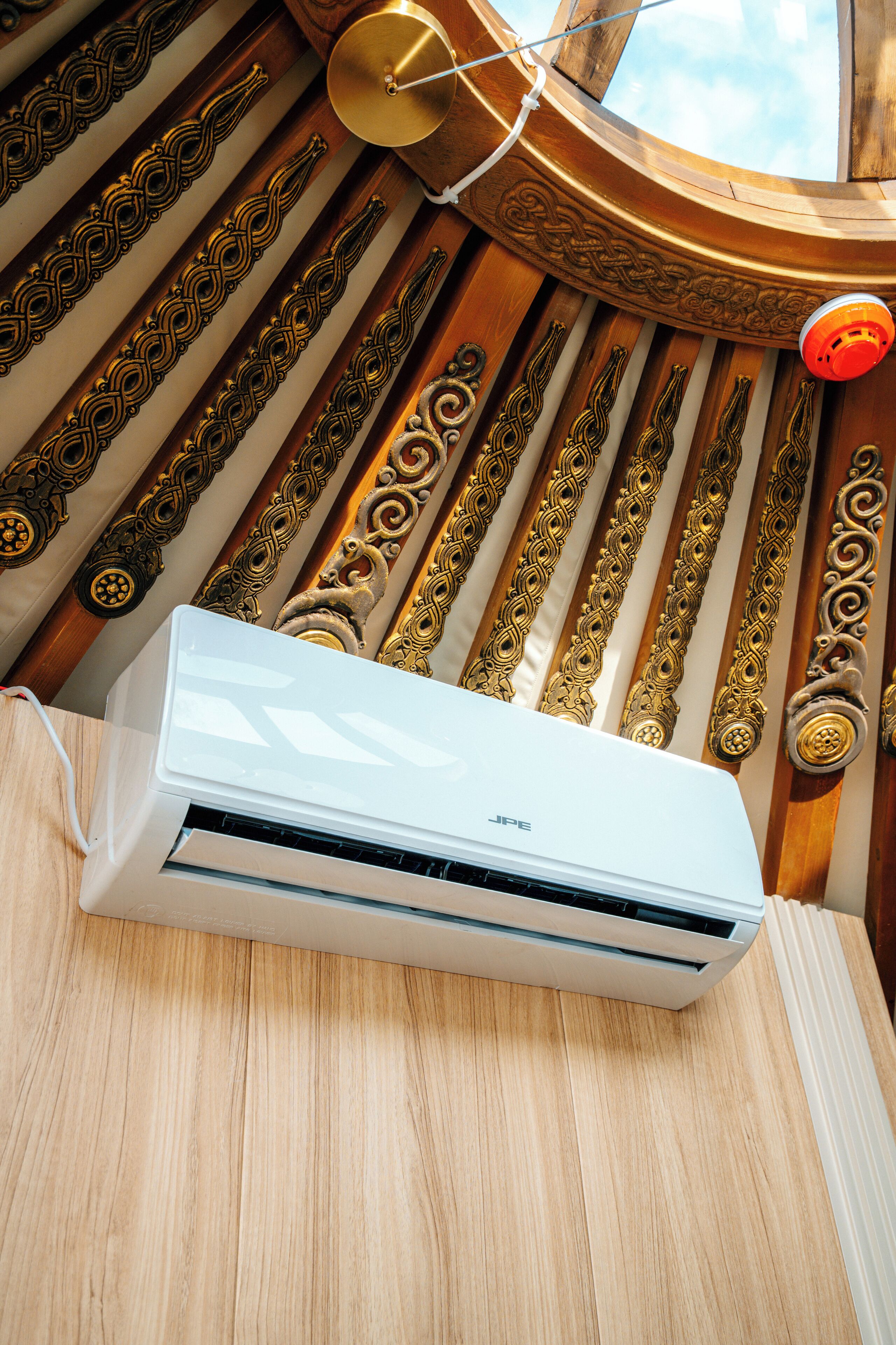 A white air conditioning unit on a wooden surface with ornate metal handles and a circular window above.