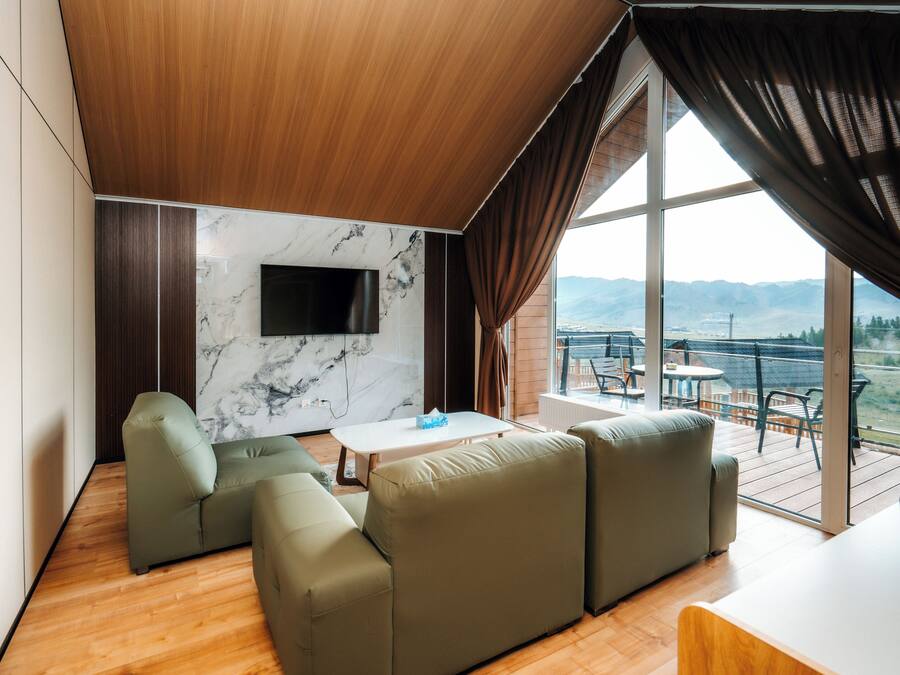 Una sala de estar moderna con techo de madera, pared de mármol y un gran ventanal con vistas a las montañas.