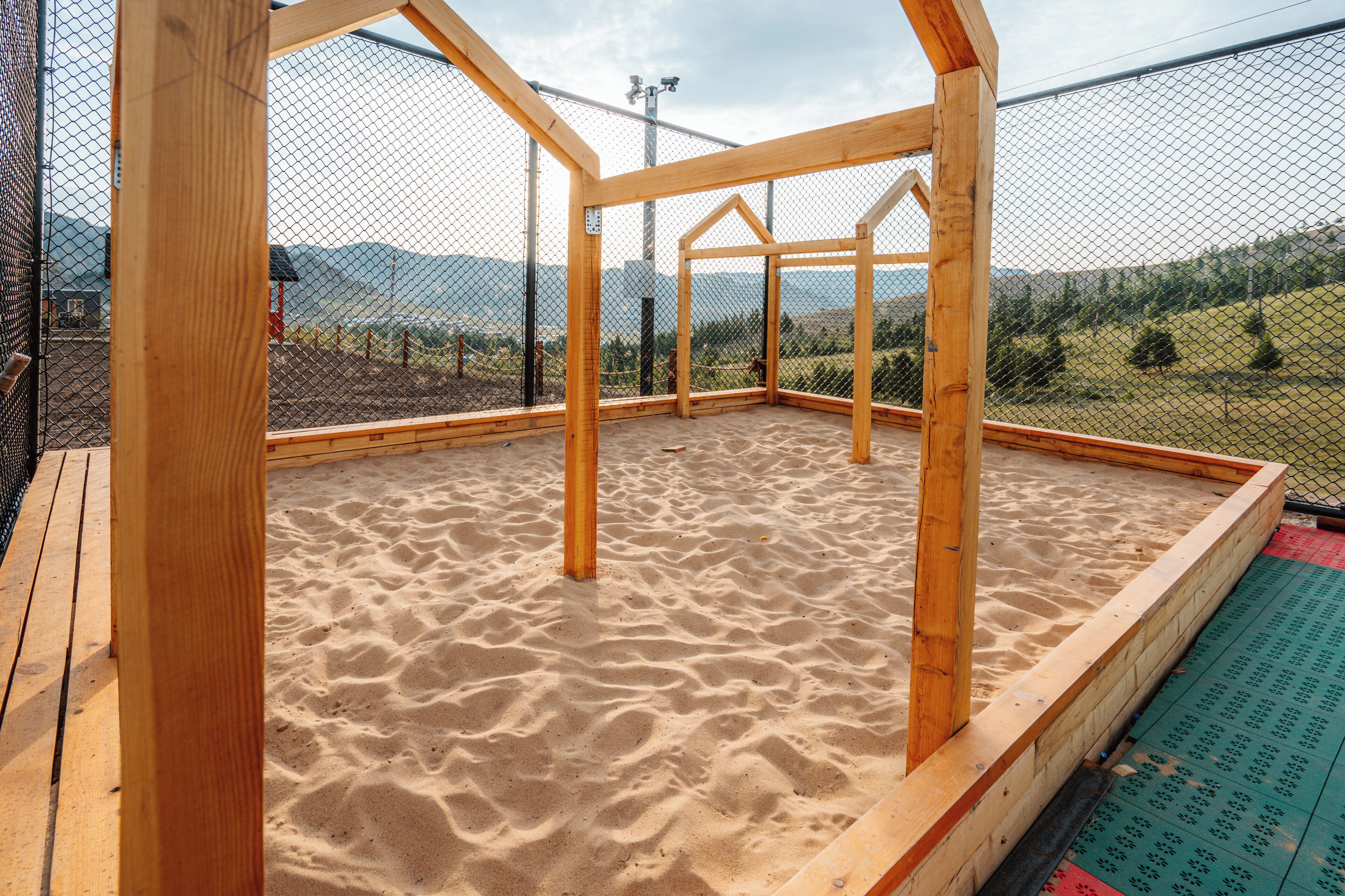 Una estructura de madera con suelo de arena, rodeada por una cerca, con vistas a un paisaje montañoso.