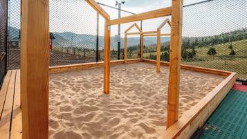 Una estructura de madera con suelo de arena, rodeada por una cerca, con vistas a un paisaje montañoso.