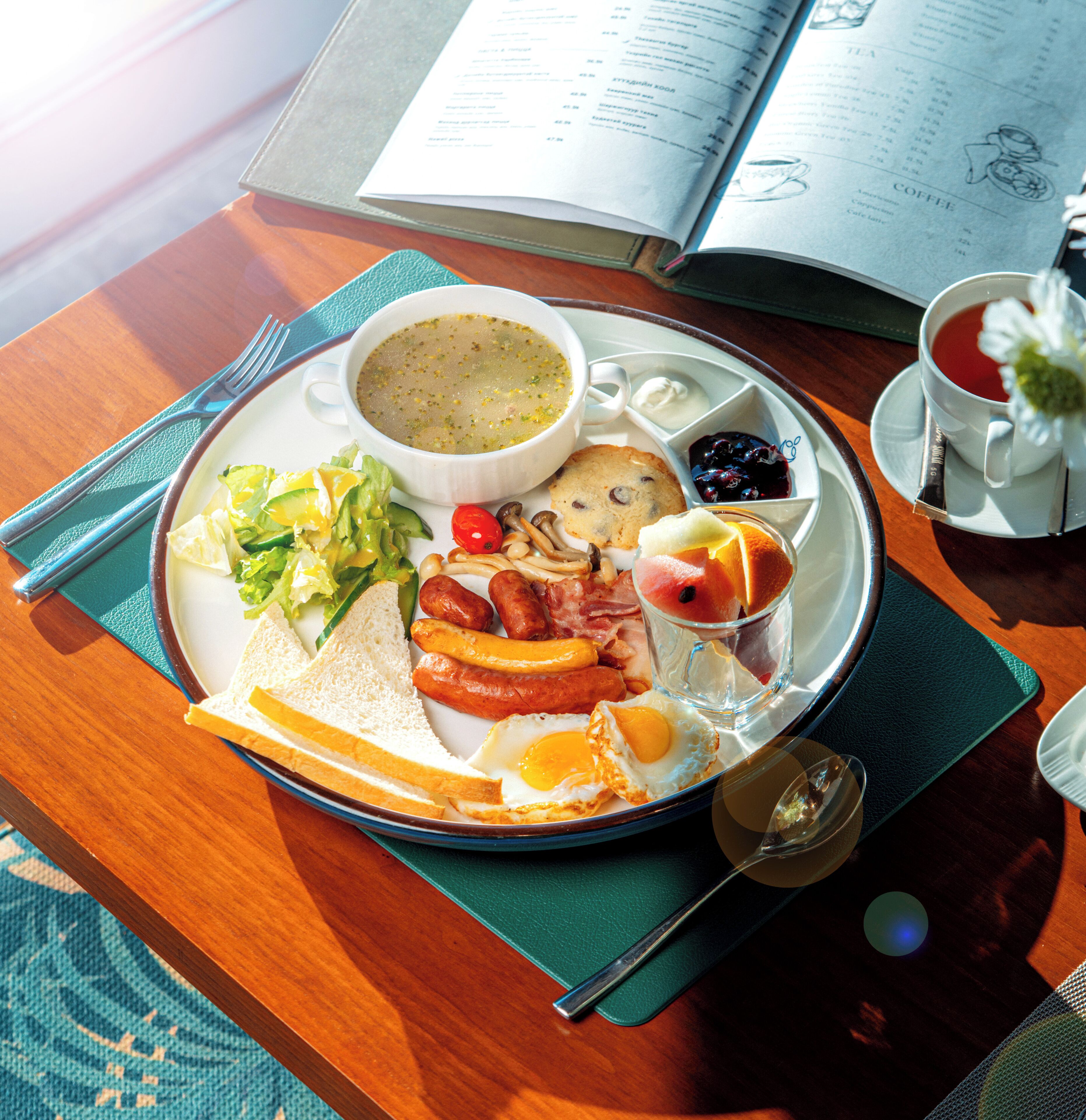 A breakfast tray with eggs, sausages, toast, and a cup of tea, placed on a table with a book and a menu.