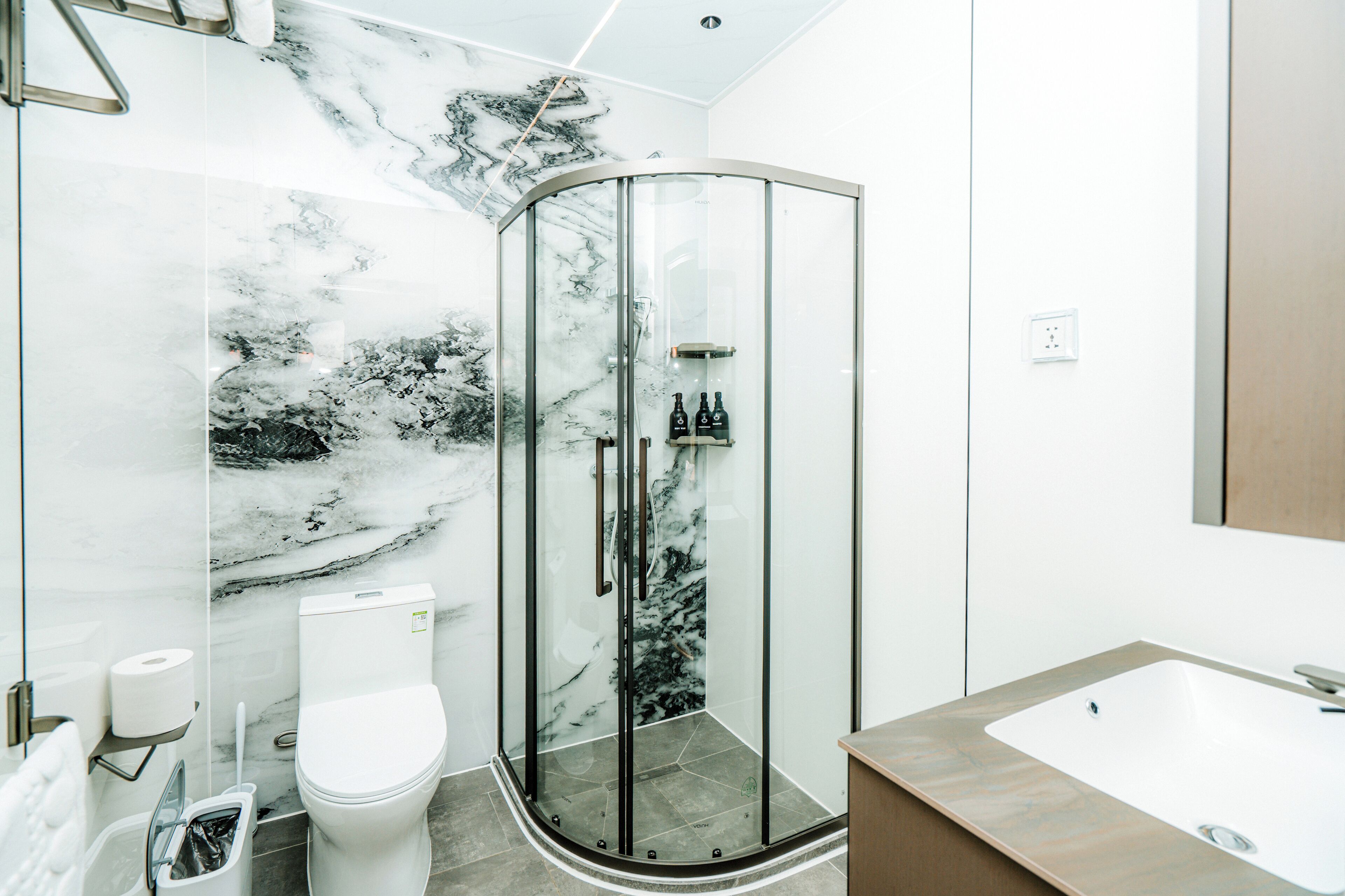 A modern bathroom with a glass shower enclosure, a toilet, and a sink.