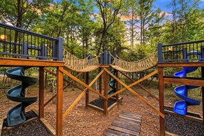 A playground with a rope bridge, spiral slides, and wooden platforms.