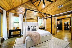 Un dormitorio con cama con dosel, techo de madera y un amplio ventanal con cortinas.