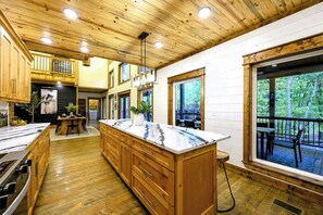 A spacious kitchen with wooden cabinets, a marble island, and large windows offering a view of the outdoors.