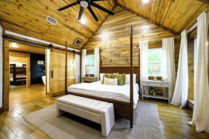 A spacious bedroom with a large bed, a wooden ceiling, and a view of the outdoors through a window. - 6 Bed, 4.5 Bath, Pool, Sauna, Hot Tub, Games, Pets (Broken Bow)