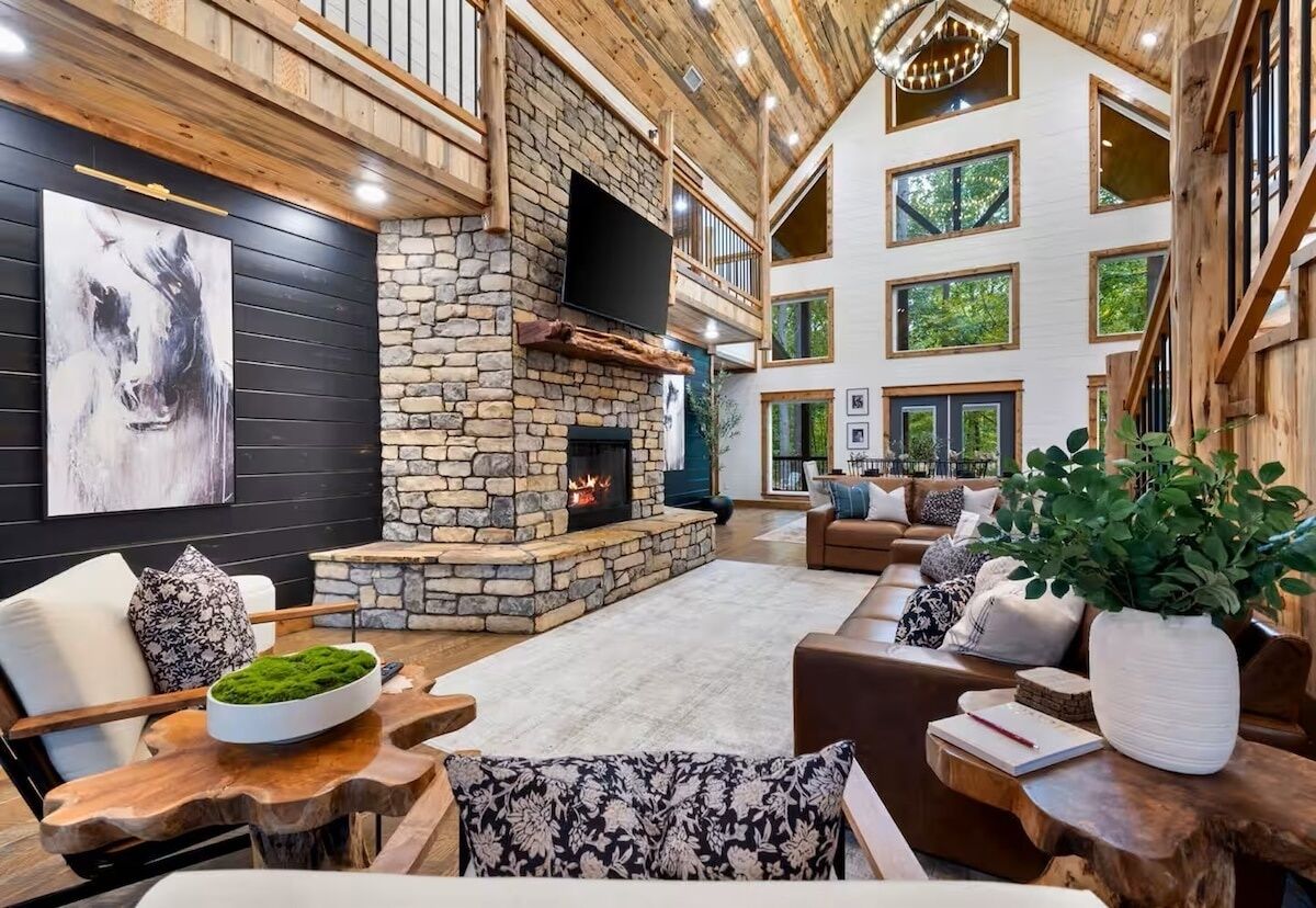 Un espacio habitable espacioso con chimenea de piedra, techo de madera y ventanas grandes.